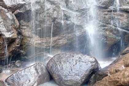 Water cascading from a height and dropping down at the rocks, providing a scenic view.