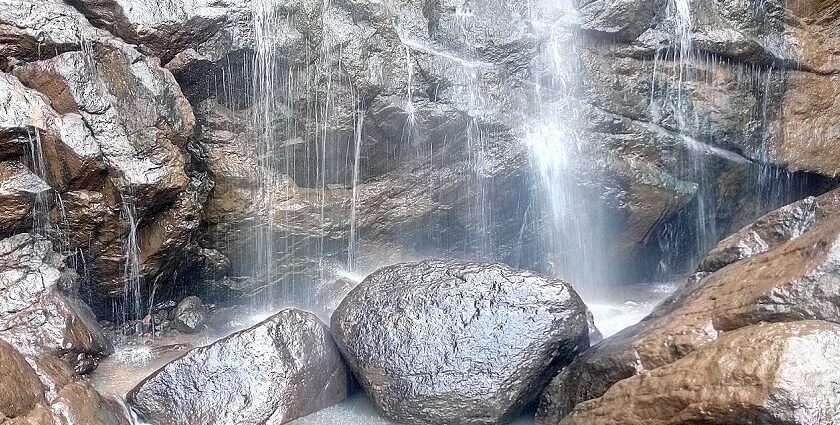 Water cascading from a height and dropping down at the rocks, providing a scenic view.