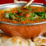 A mouth-watering view of a bowl served with a cooked dish and flatbreads on the side.