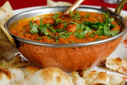 A mouth-watering view of a bowl served with a cooked dish and flatbreads on the side.