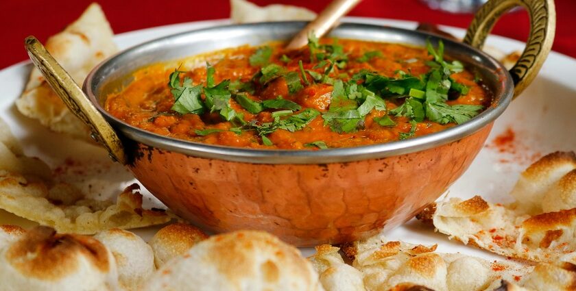 A mouth-watering view of a bowl served with a cooked dish and flatbreads on the side.