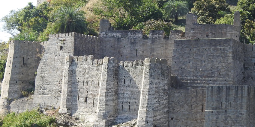 Kangra fort in Himachal Pradesh with its tall and grey stone walls in under the sun.