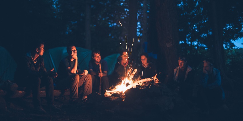 People sitting around a bonfire, playing games and singing songs