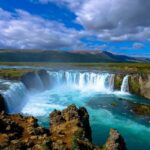 A picture of a serene waterfall with a mountainous view in the background on a cloudy day