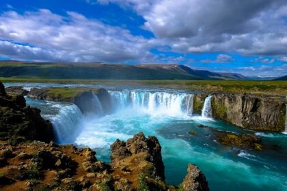 A picture of a serene waterfall with a mountainous view in the background on a cloudy day