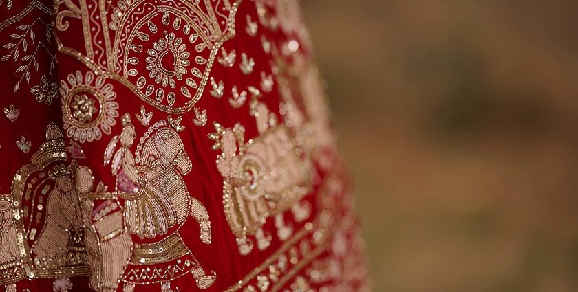 A glimpse of a bright red coloured bridal attire adorned with golden embroidery.