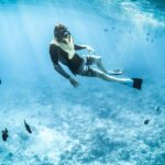 A glimpse of a person diving deep in the azure ocean exploring the marine life underwater.