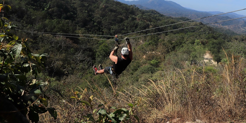 A man ziplining through the air over a lush green forest canopy in a tropical setting.
