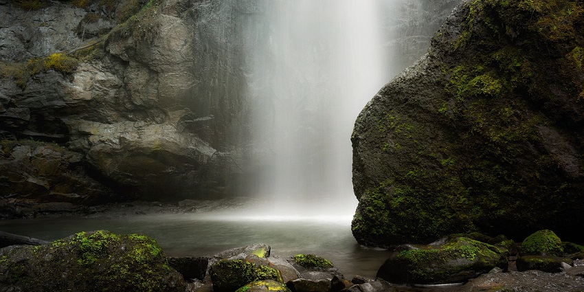 Majestic waterfall cascading down lush green rocks surrounded by dense forest.