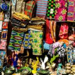 Colourful handicrafts, bags, ceramic plates, and earrings being sold in a market.