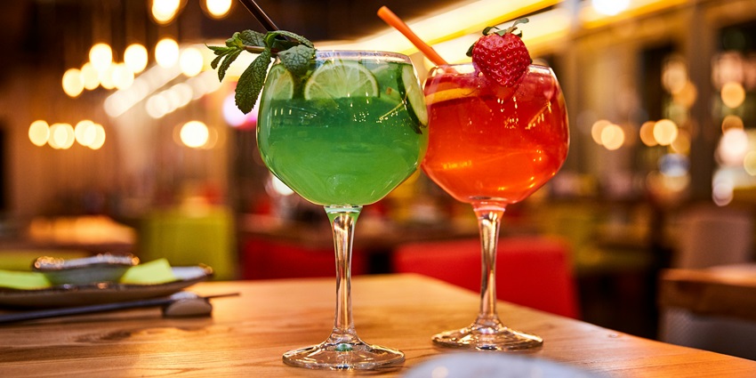 Image of two clear glasses with fruit drinks green and red a strawberry and lemon on the glasses