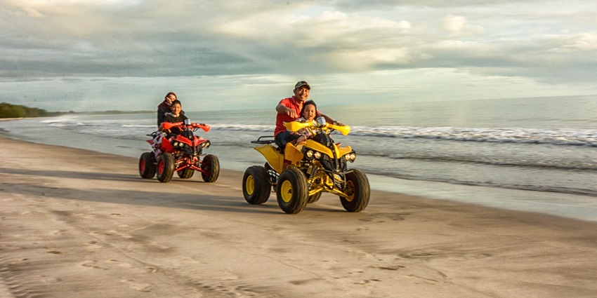 A picture of tourists enjoying ATV bike rides at a beach with views of the sea in background