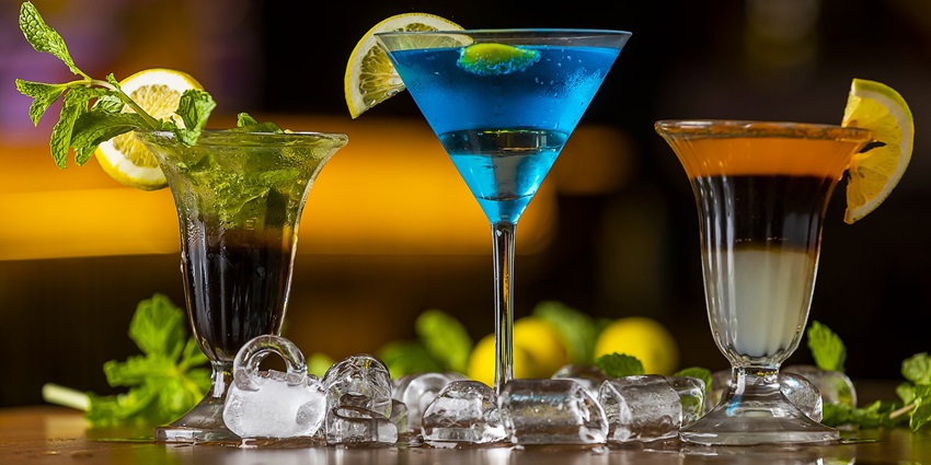 Three colorful cocktails with fruit garnishes on a table, set against a blurred background