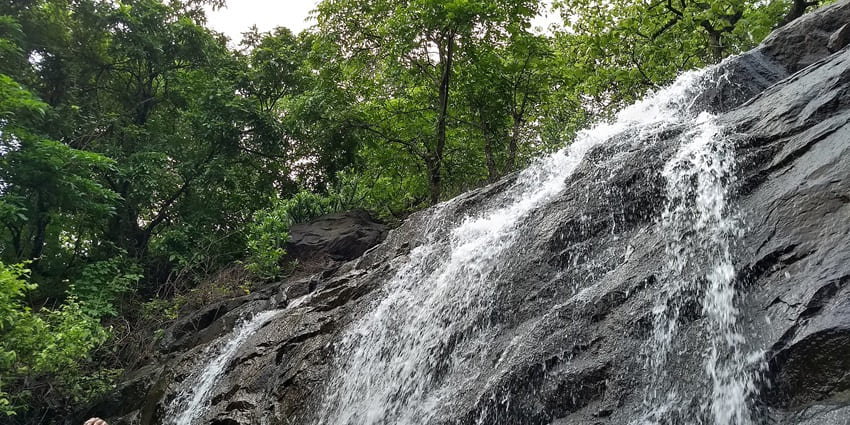 Picturesque view of Aashti Waterfall surrounded by rocky terrain and greenery showcasing flowing water.