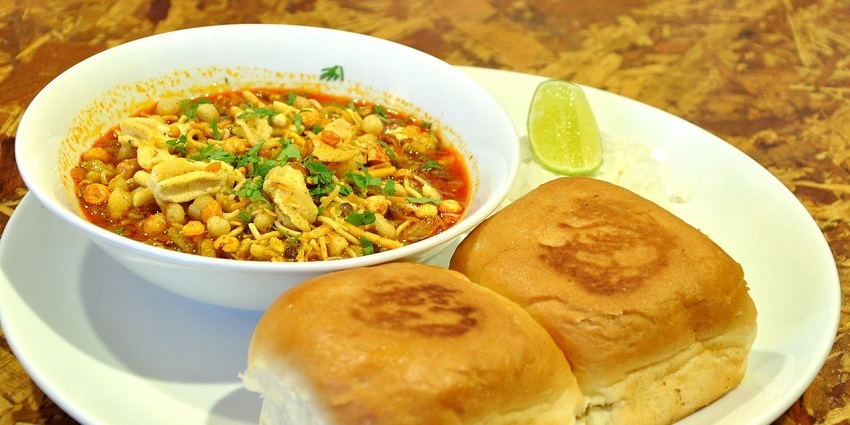 Misal topped with farsan, served with soft pav bread, onions, and lemon on the side