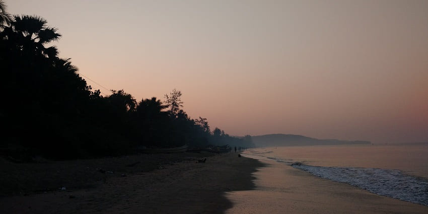 A unset view of Achra Beach with calm waters and golden sandy shore.