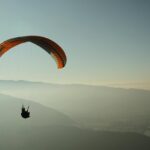 A glimpse of a person gliding high up in the air surrounded by majestic peaks.