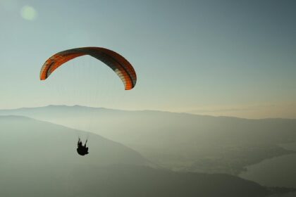 A glimpse of a person gliding high up in the air surrounded by majestic peaks.