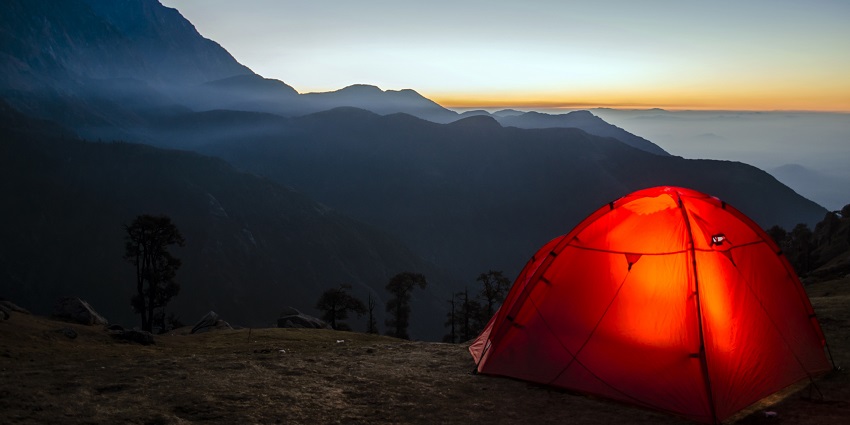 An orange-coloured tent is located on the edge of a hill while sunrise is taking place