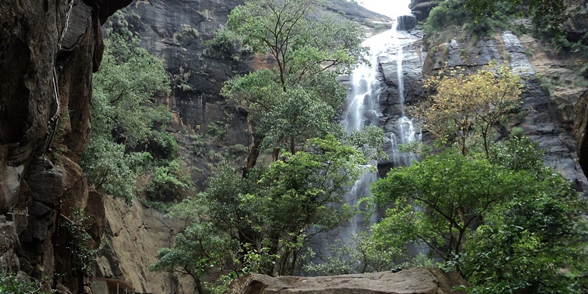 Scenic Agaya Gangai waterfall cascading over rocky terrain, surrounded by lush greenery.