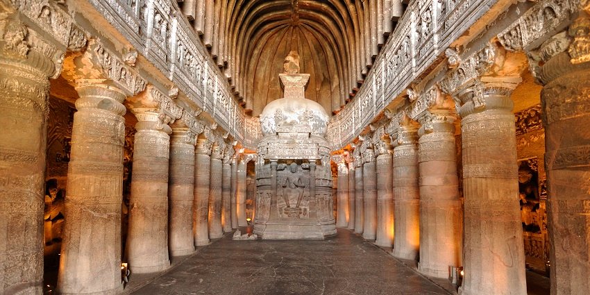 An image of Ajanta Caves nestled in a horseshoe-shaped cliff with lush greenery.