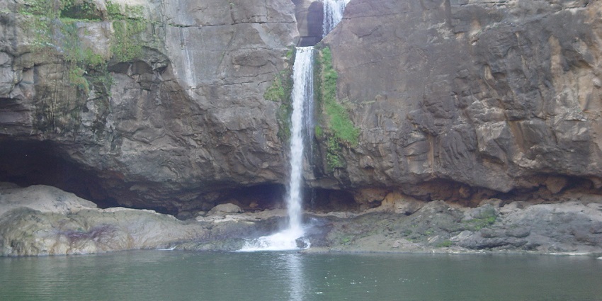A scenic view of the Ajanta Caves showcases ancient rock-cut architecture with a waterfall surrounded by greenery.