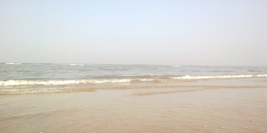 Calm waves lapping gently on the sandy shoreline of Aksa Beach under a clear sky