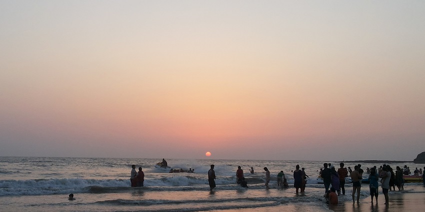 Sunset over Alibaug Beach with vibrant orange and purple hues reflecting on the water.