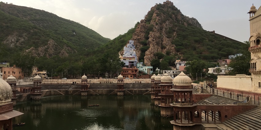 A majestic view of the Moosi Maharani ki Chhatri with a pond in front of it and hills in the background
