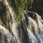 A view of shimmering waters cascading down from the rocky cliffs decked with greenery.