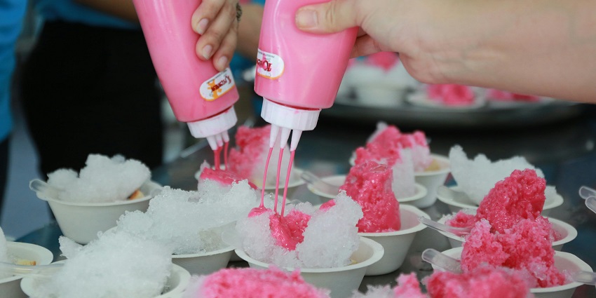 Vendor pouring a pink coloured flavoured syrup on the freshly shaved ice placed in a bowl