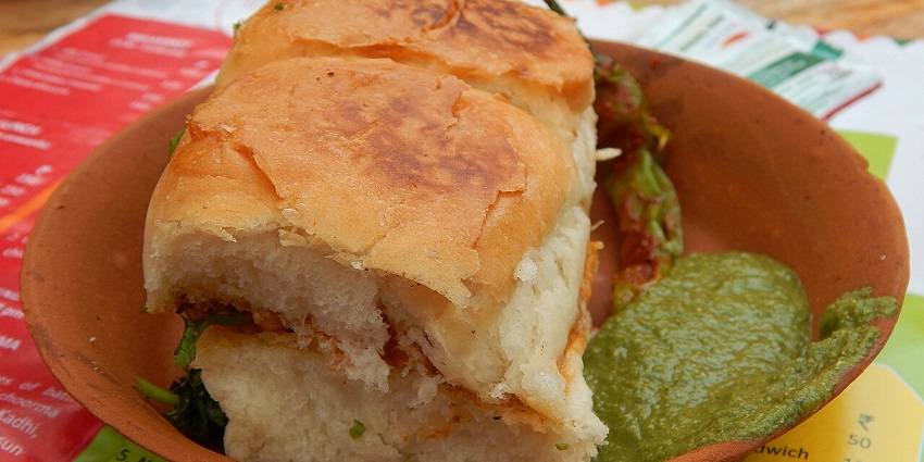 Street-style vada pav with spicy chutney and a green chilli served in a clay utensil
