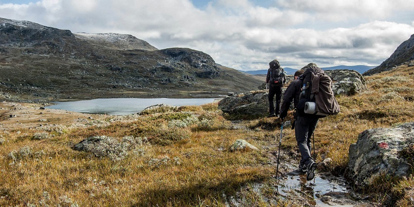 A hiker wearing a backpack and holding trekking poles stands on a rocky mountain trail