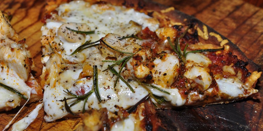 A Roasted Chicken Pizza, topped with cheese, herbs and spices served on a wooden plate.