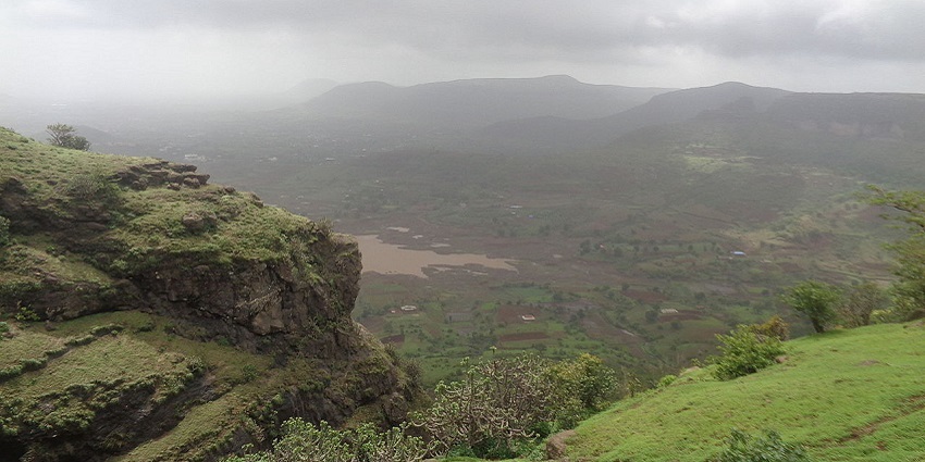 Green hills with rugged terrain and sparse trees under a bright blue sky with scattered clouds