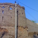 Anupgarh Fort’s sandstone walls rise against a clear blue sky with two people outside.