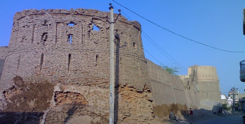 Anupgarh Fort’s sandstone walls rise against a clear blue sky with two people outside.