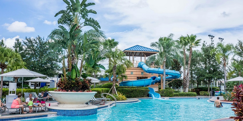 Picturesque view of a people on swimming pool area near a resort and trees around