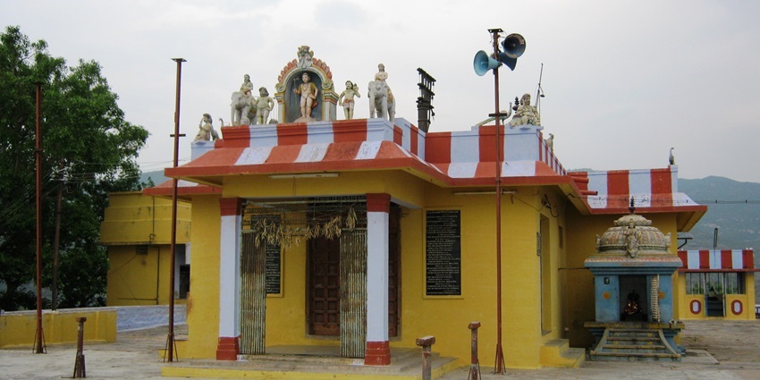 A frontal view of a traditional Hindu temple with bright yellow walls and idols of deities on roof.