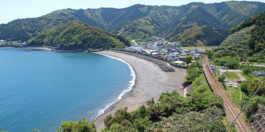 A small rural train station surrounded by a scenic natural setting with a lone railway track