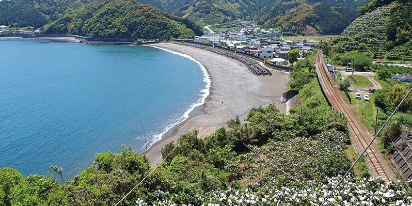 A small rural train station surrounded by a scenic natural setting with a lone railway track