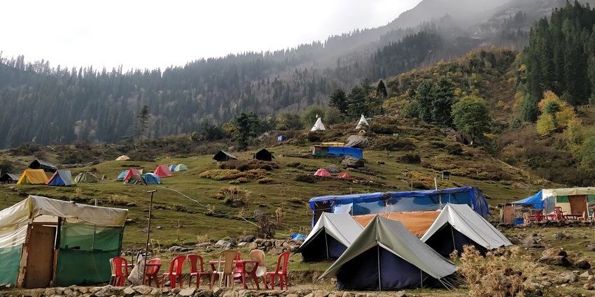 Several tents are placed on a small hill on the side of the tents there are red chairs