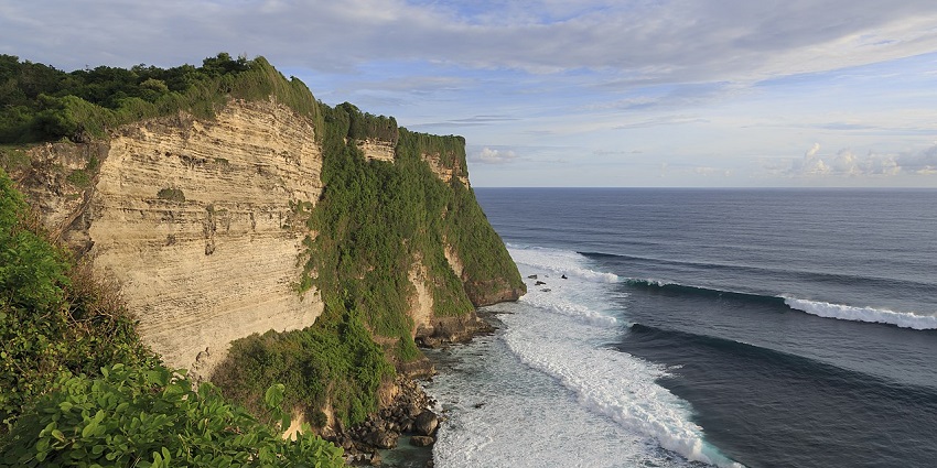 Cliffs of Pura Luhur Uluwatu overlooking the ocean with hard waves at sunset in Bali.