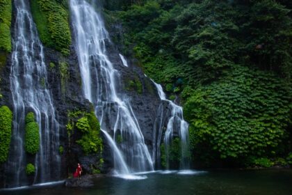 An aerial view of cascading waterfalls surrounded by lush green forests and rocky terrain.