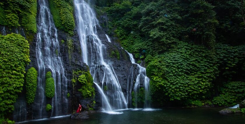 An aerial view of cascading waterfalls surrounded by lush green forests and rocky terrain.