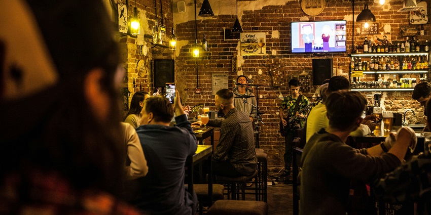 People seated around a bar, illuminated by warm lights, in a casual evening setting.