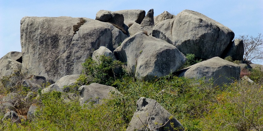 A rock pile under a clear sky surrounded by green bushes near the Nagarjuni Caves.
