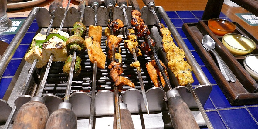 Image of skewers such as veggies, cottage cheese and meats on a grill at Barbeque Nation.
