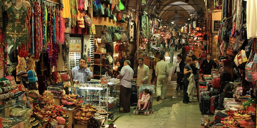 Image of shops in a Grand Bazaar displaying colourful textiles, lanterns, and ceramics