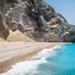 A beautiful beach scene with clear blue water, soft white sand, and a vibrant green island in the background.